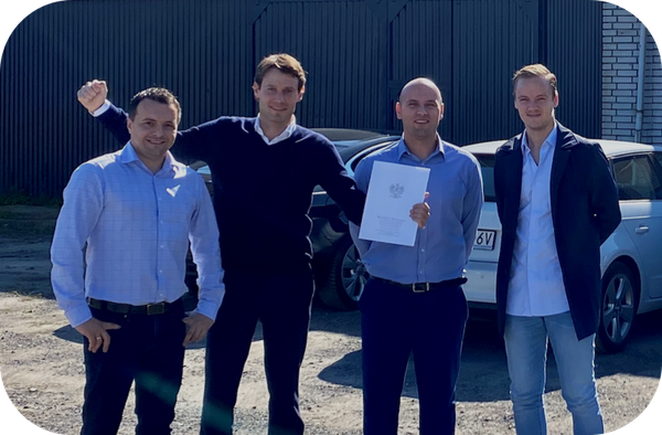 Several men standing outdoors in front of an industrial building, holding a document toward the camera – photograph marking the establishment of the new site in Poland.